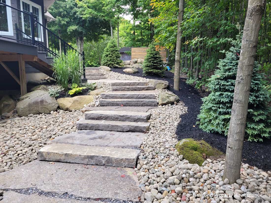 Stone stepping stairs leading up a landscaped garden path beside a house with a deck on the left and pebble ground cover