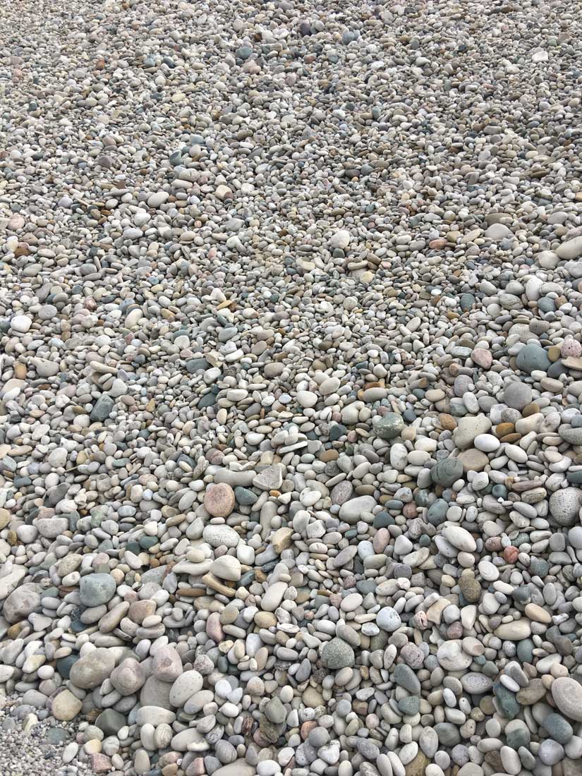 Close-up view of many smooth, rounded pebbles in various pastel colors covering the ground (pebble beach/shore).