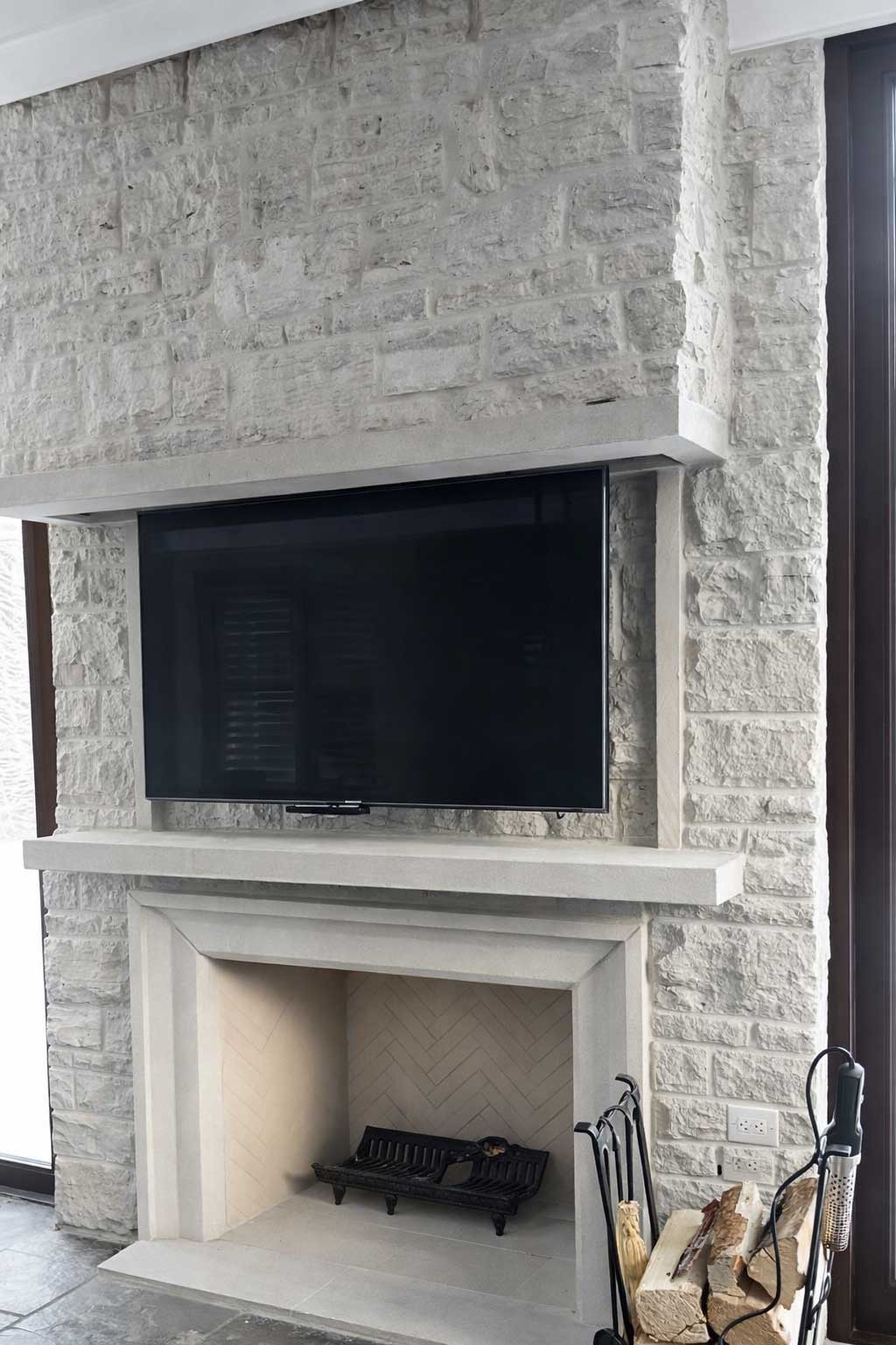Flat-screen TV mounted over a stone fireplace with a white mantel and built-in hearth in a bright living room setting.
