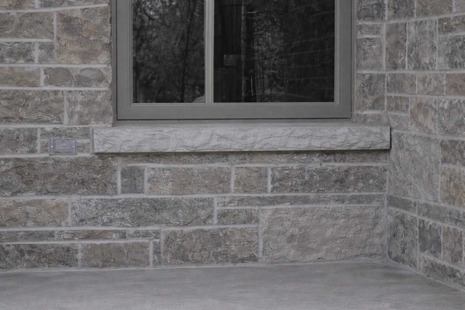 Stone exterior wall with a rectangular window and a marble-like windowsill; a small metal utility box is mounted to the left.